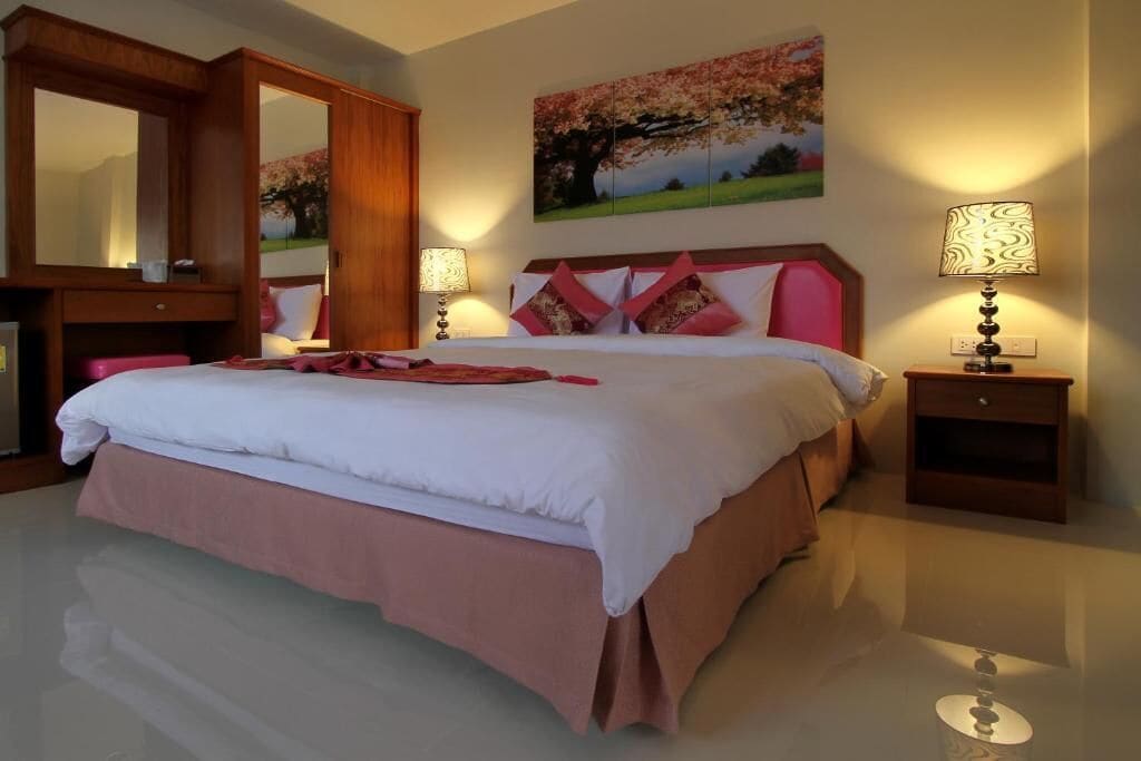 A spacious bedroom with a large bed, a wooden wardrobe, a bedside table with a lamp, and a painting on the wall.