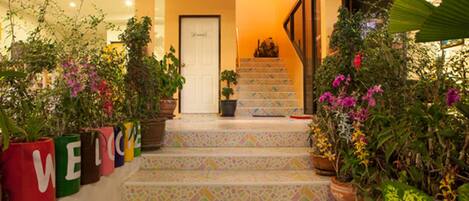 A staircase with colorful tiles leading to a door, surrounded by potted plants and a 'WELCOME' sign.