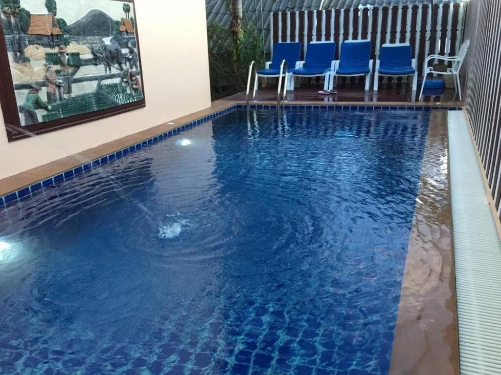 Piscina interior com água azul cristalina, rodeada por cadeiras azuis e uma moldura de azulejos.
