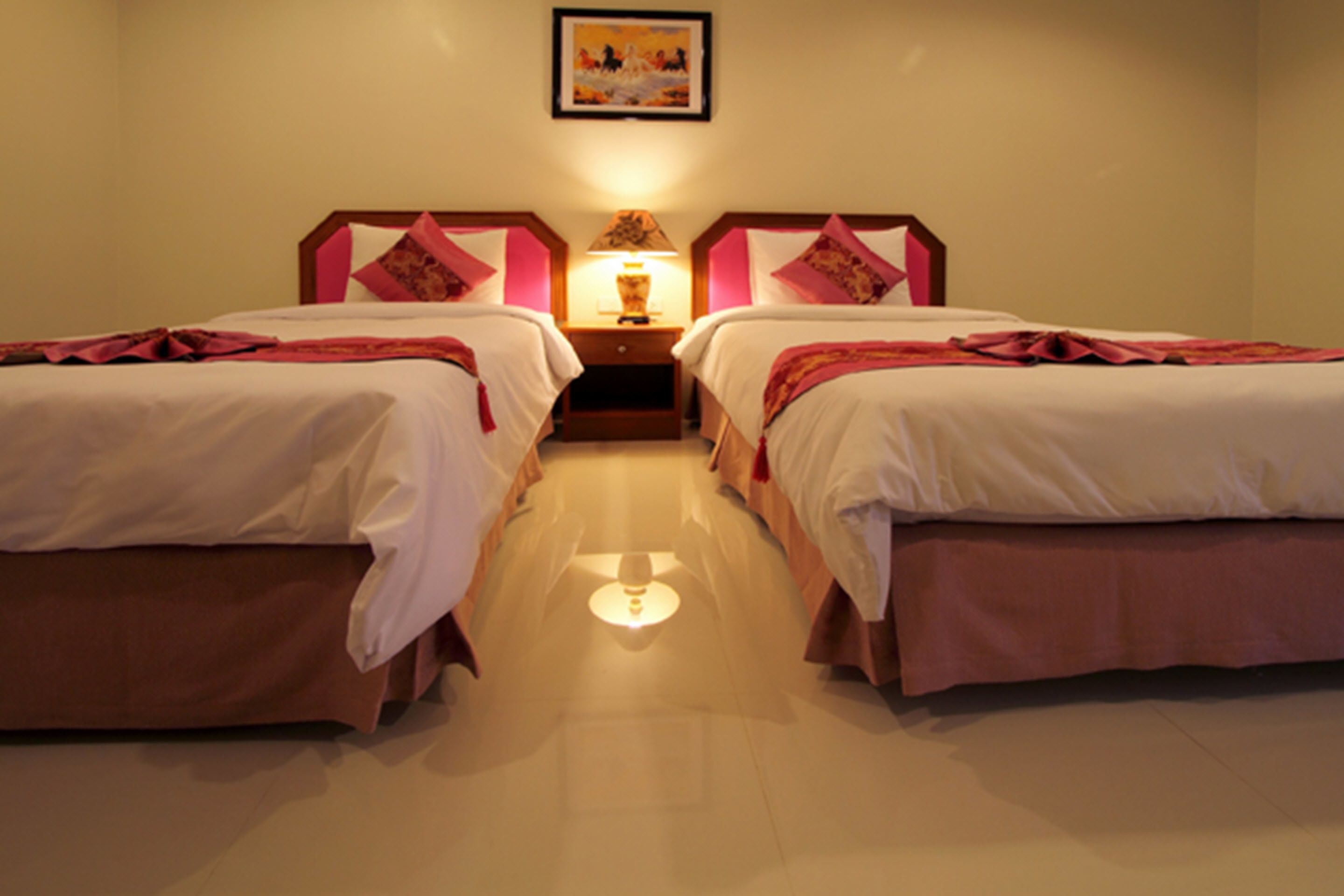 Habitación de hotel con dos camas individuales, una mesita de noche con lámpara y un cuadro enmarcado en la pared.