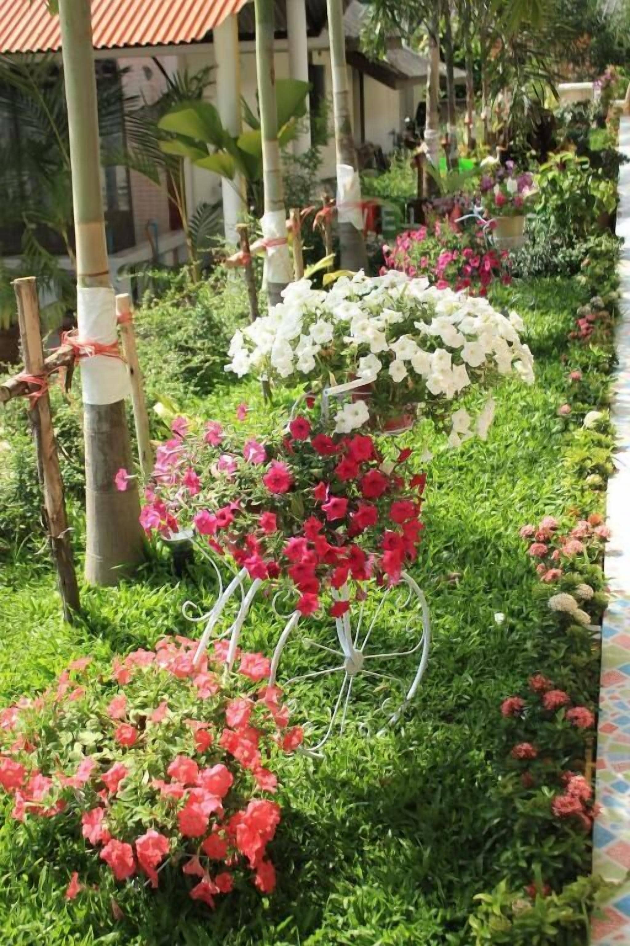 Un jardin agrémenté de différents parterres de fleurs, dont des fleurs roses et blanches, ainsi que de structures en bambou.