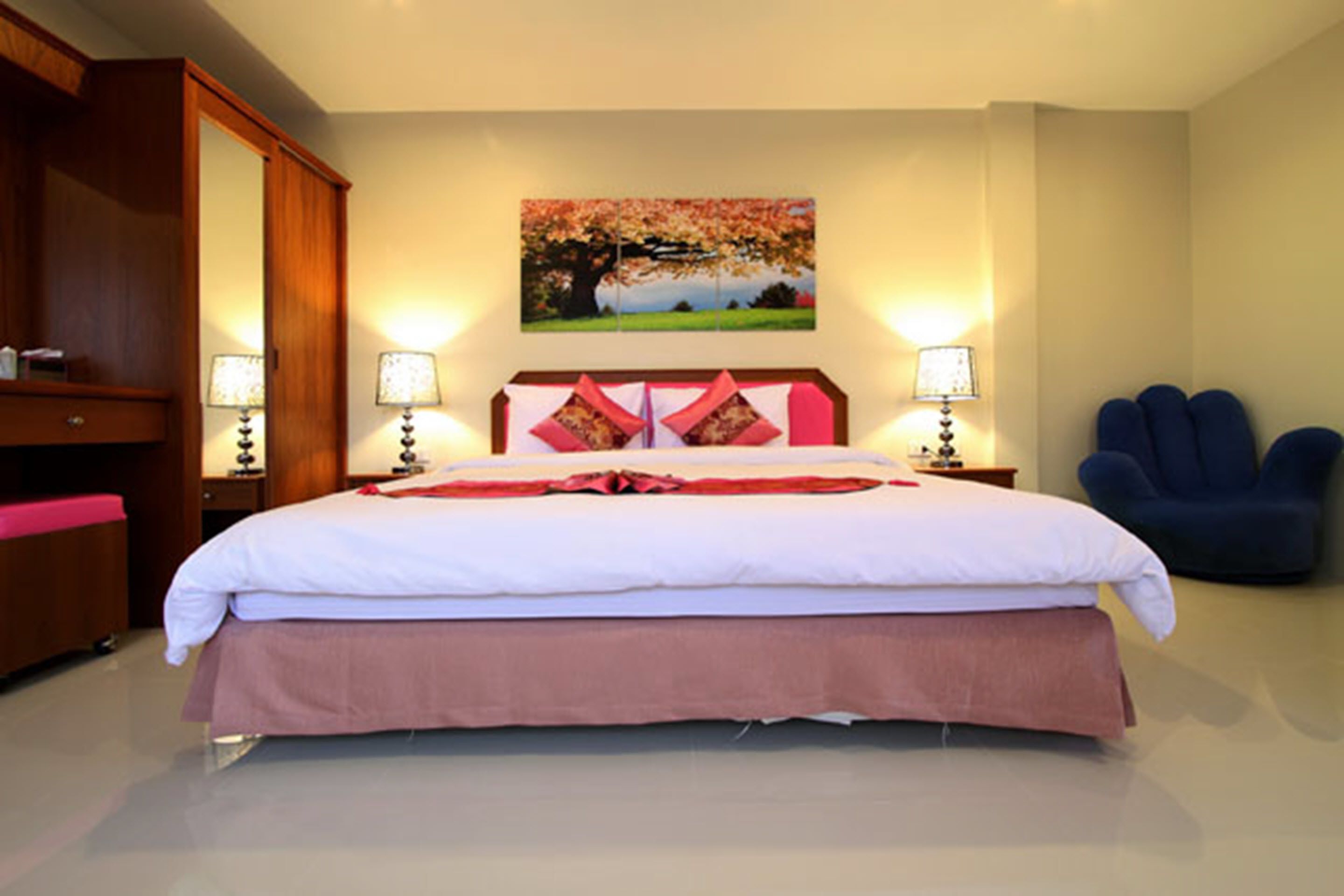 A neatly made bed with a pink skirt, two bedside lamps, and a blue chair.