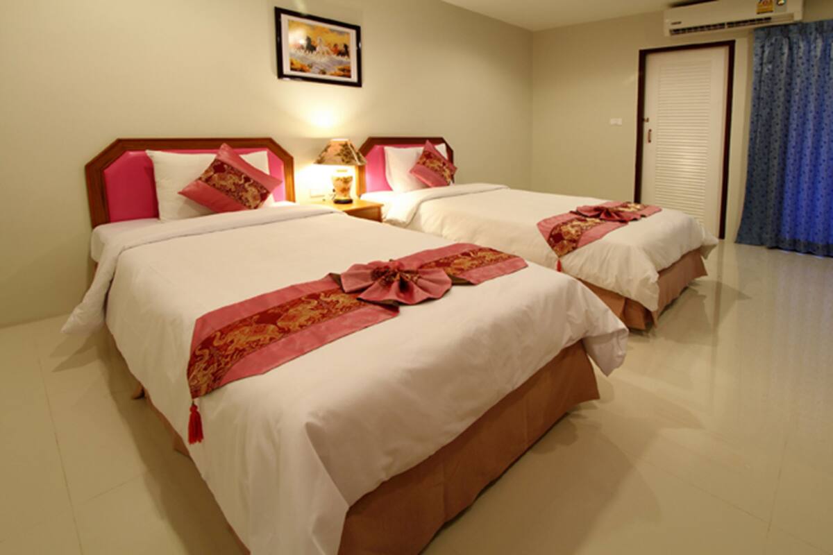 A hotel room with two beds, each with pink and white bedding, a framed picture on the wall, and a closed door with a curtain.