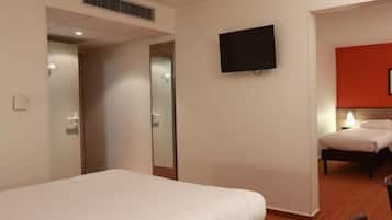 Camera d'albergo con un letto singolo, una TV a schermo piatto montata a parete, un comodino con una lampada e una parete decorata in rosso.