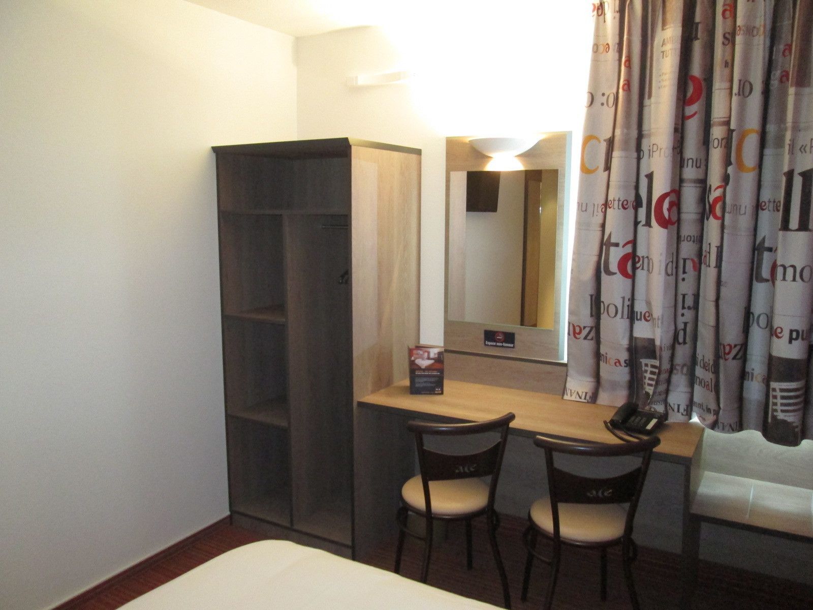 A hotel room with a bed, a desk with two chairs, a mirror, and a wardrobe.