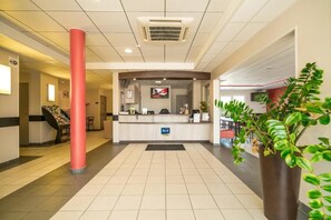 Welcome to our hotel, where guests can check in at the central reception desk, featuring a digital screen and a helpful staff member.