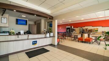 A hotel reception area with a counter, a television, and a dining area with tables and chairs.