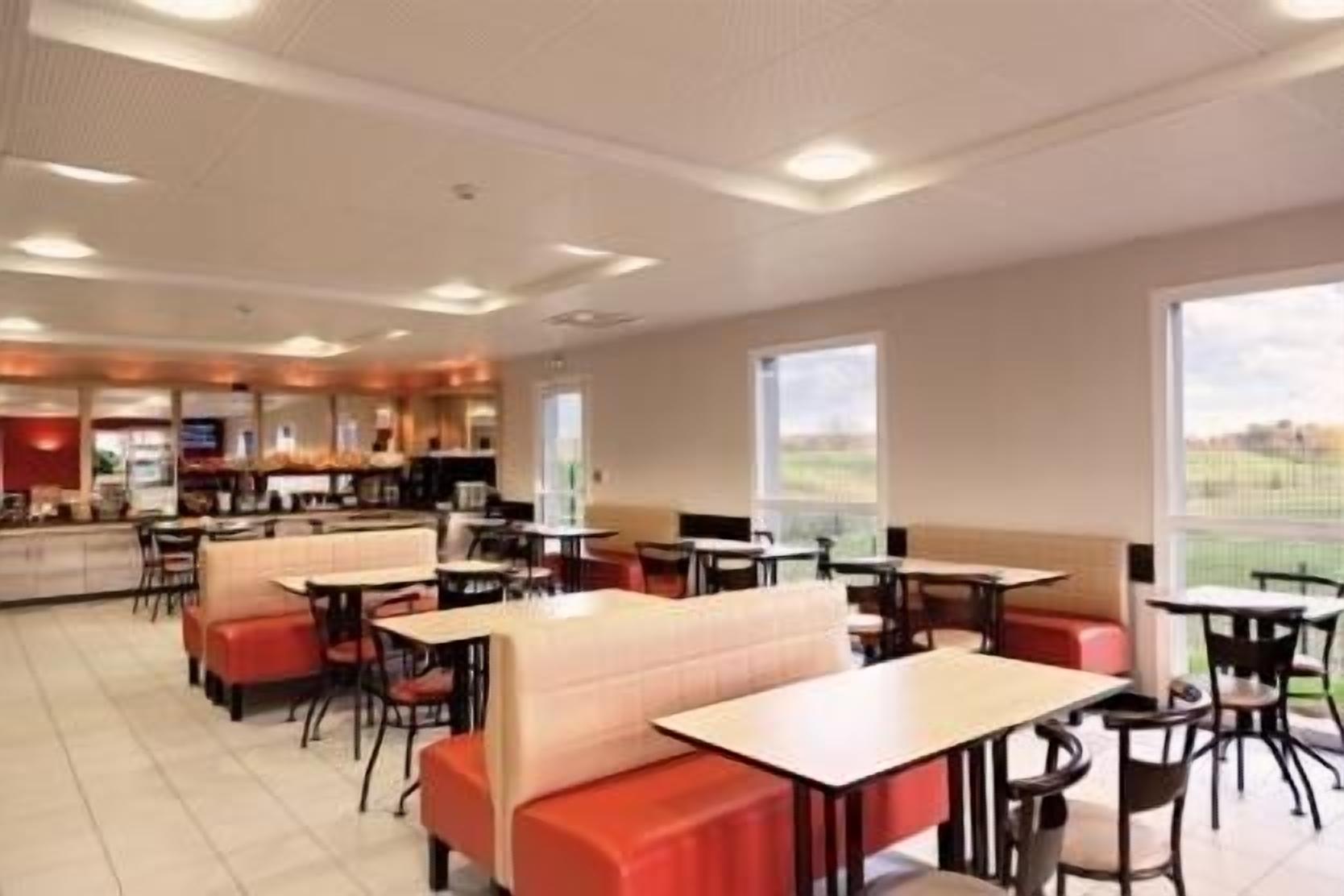 A modern restaurant with booths and tables, a kitchen area, and large windows offering a view.