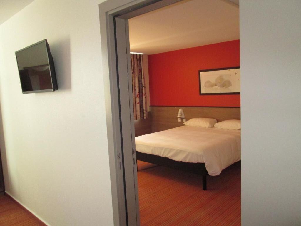 A bedroom with a bed, a wall-mounted TV, and a red accent wall.