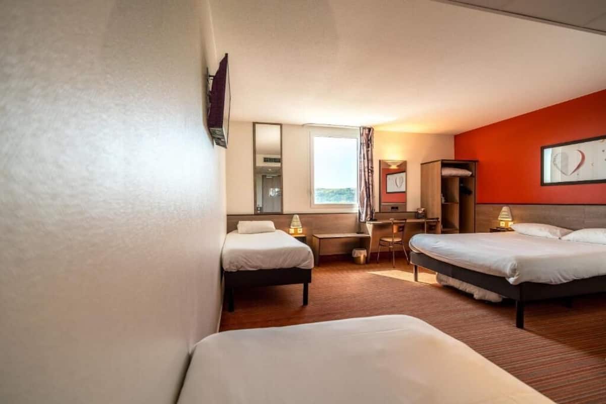 A hotel room with two beds, a desk, a chair, and a window with curtains.