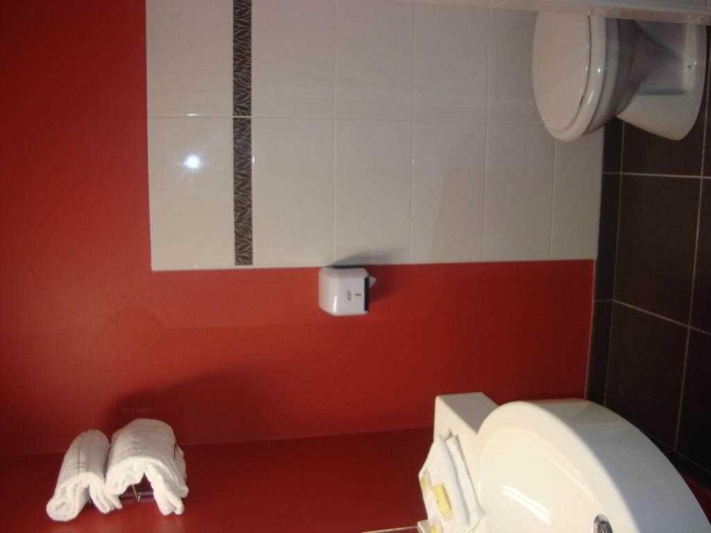 A bathroom with a red wall, white tiles, a toilet, a hand dryer, and a towel rack.
