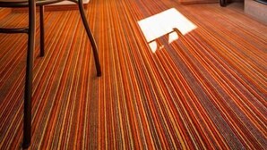 A hotel room with a striped carpet, a bed, a chair, and a nightstand with a lamp. - Ace Hôtel Valence  (Valence)