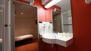 A hotel room with a single bed, a white sink with a mirror, and a red wall.