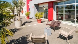 A modern building with a red and white facade, outdoor seating area with chairs and tables, and potted plants. - Ace Hôtel Valence  (Valence)