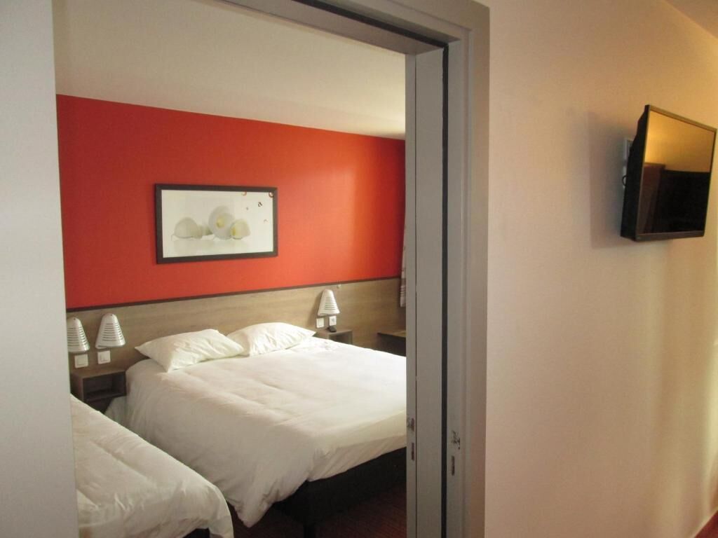 Een hotelkamer met twee bedden, een rode accentmuur, een ingelijste foto, bedlampen en een aan de muur bevestigde televisie.