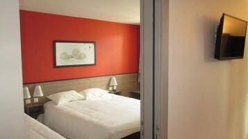 A hotel room with two beds, a red accent wall, a framed picture, bedside lamps, and a TV mounted on the wall.