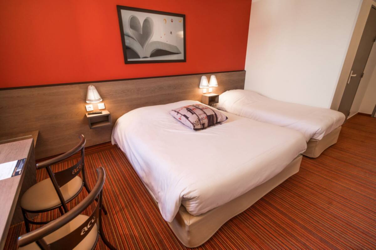A hotel room with a bed, bedside lamps, a chair, and a wall-mounted picture.