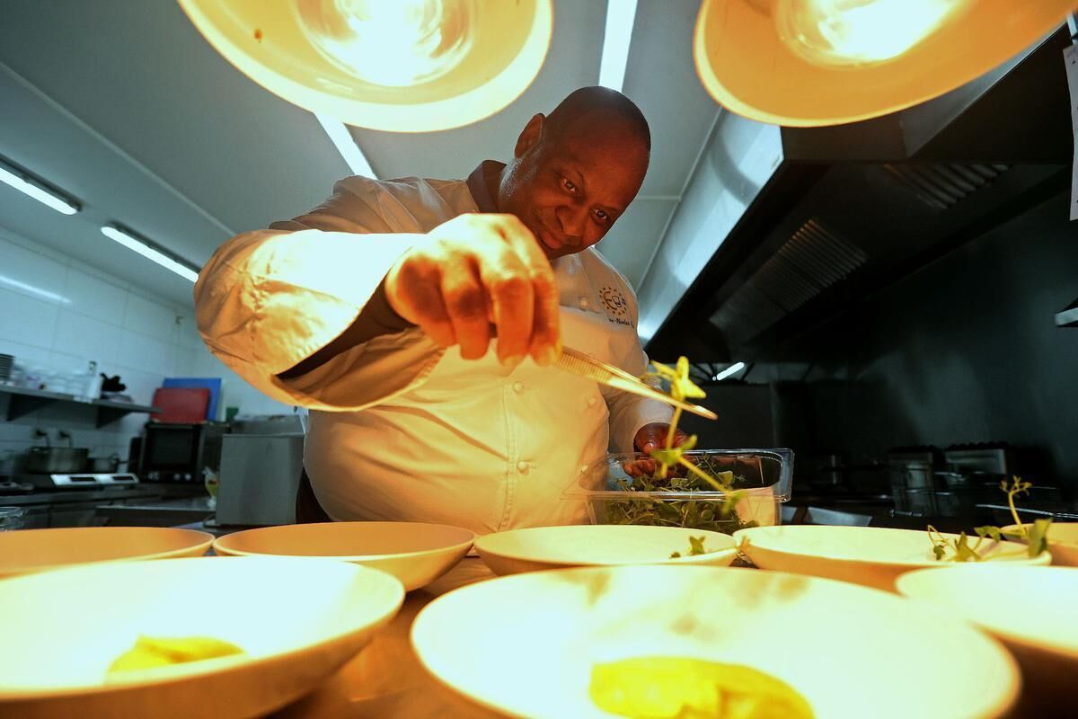 A chef preparing food in a professional kitchen with multiple bowls and cooking equipment.