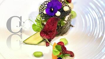 Ein weißer Teller mit einem Sushi-Rolle, belegt mit einer violetten Blume, grünen Blättern und kleinen, weißen Kugeln.