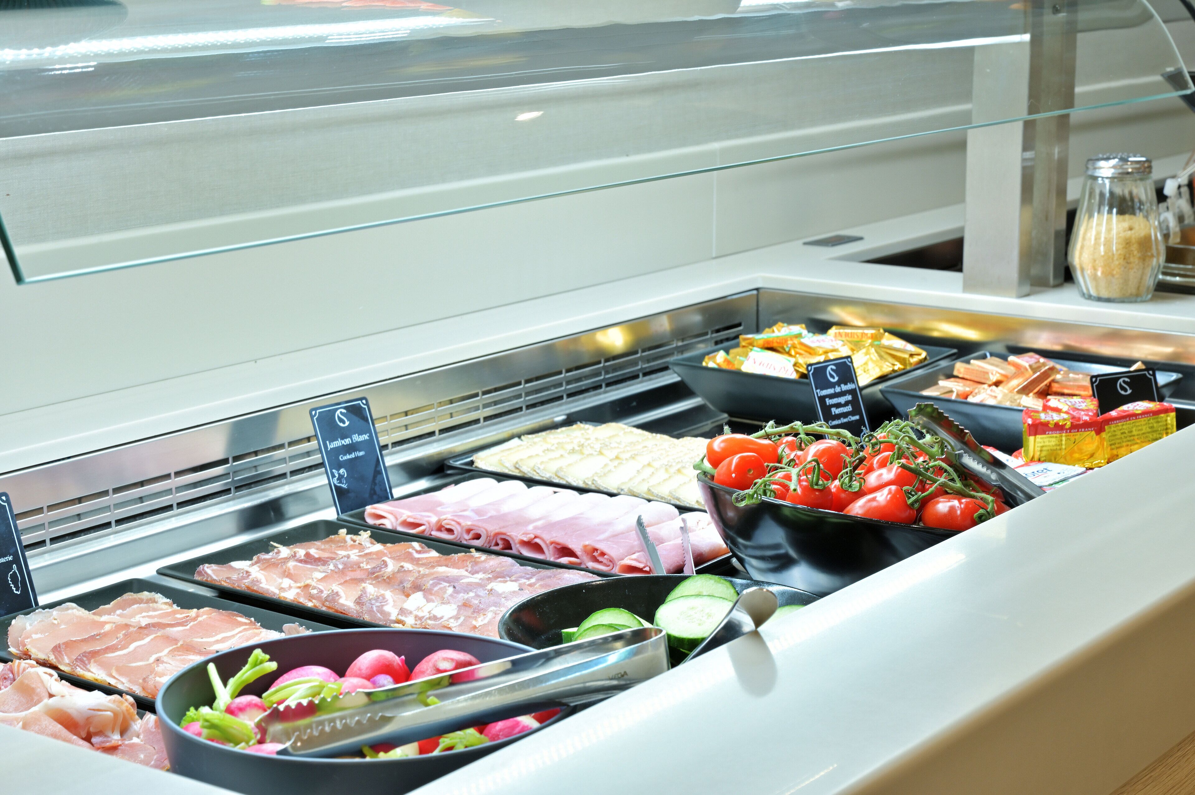 A deli counter with various meats, cheeses, and vegetables.
