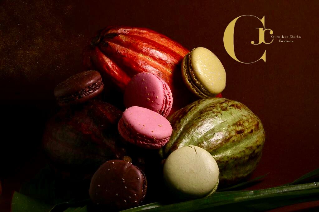 A variety of macarons and a chocolate-covered fruit on a dark surface.
