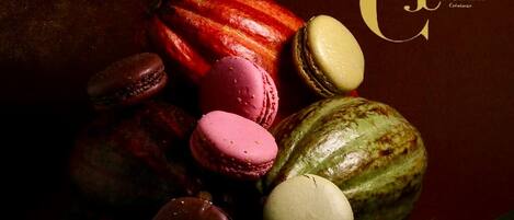 A variety of macarons and a chocolate-covered fruit on a dark surface.