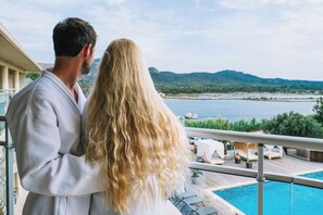 Una pareja en un balcón con vista a una piscina, un lago y montañas.