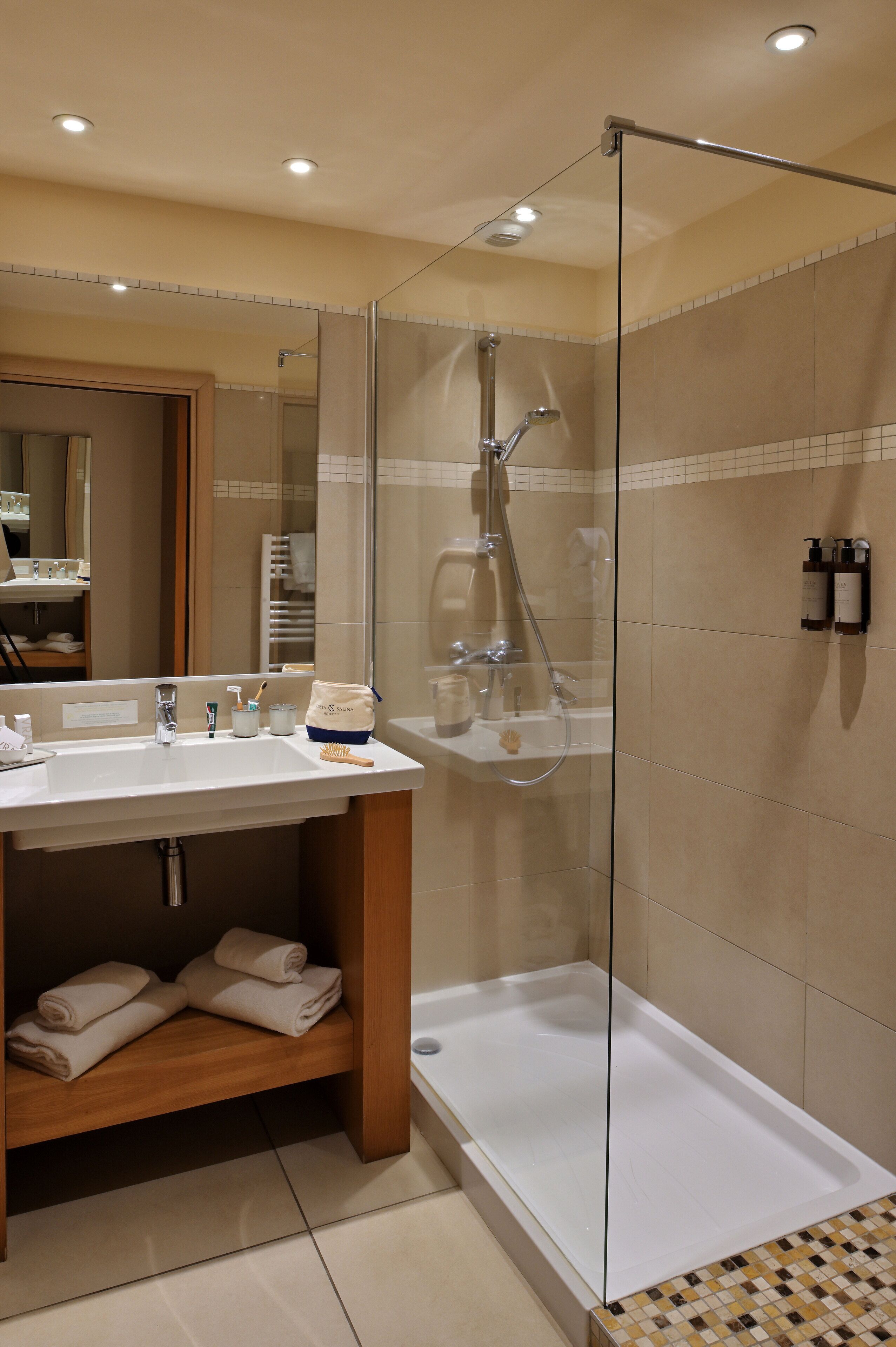 Un bagno moderno con cabina doccia in vetro, lavandino bianco e ripiano in legno con asciugamani.