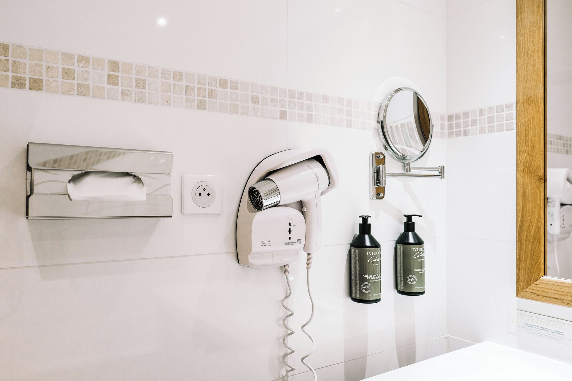 A bathroom with a hairdryer, two bottles of shampoo, a towel dispenser, and a mirror.