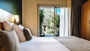 A hotel room with a large bed, a nightstand with a lamp, and a view of a garden through a sliding glass door.