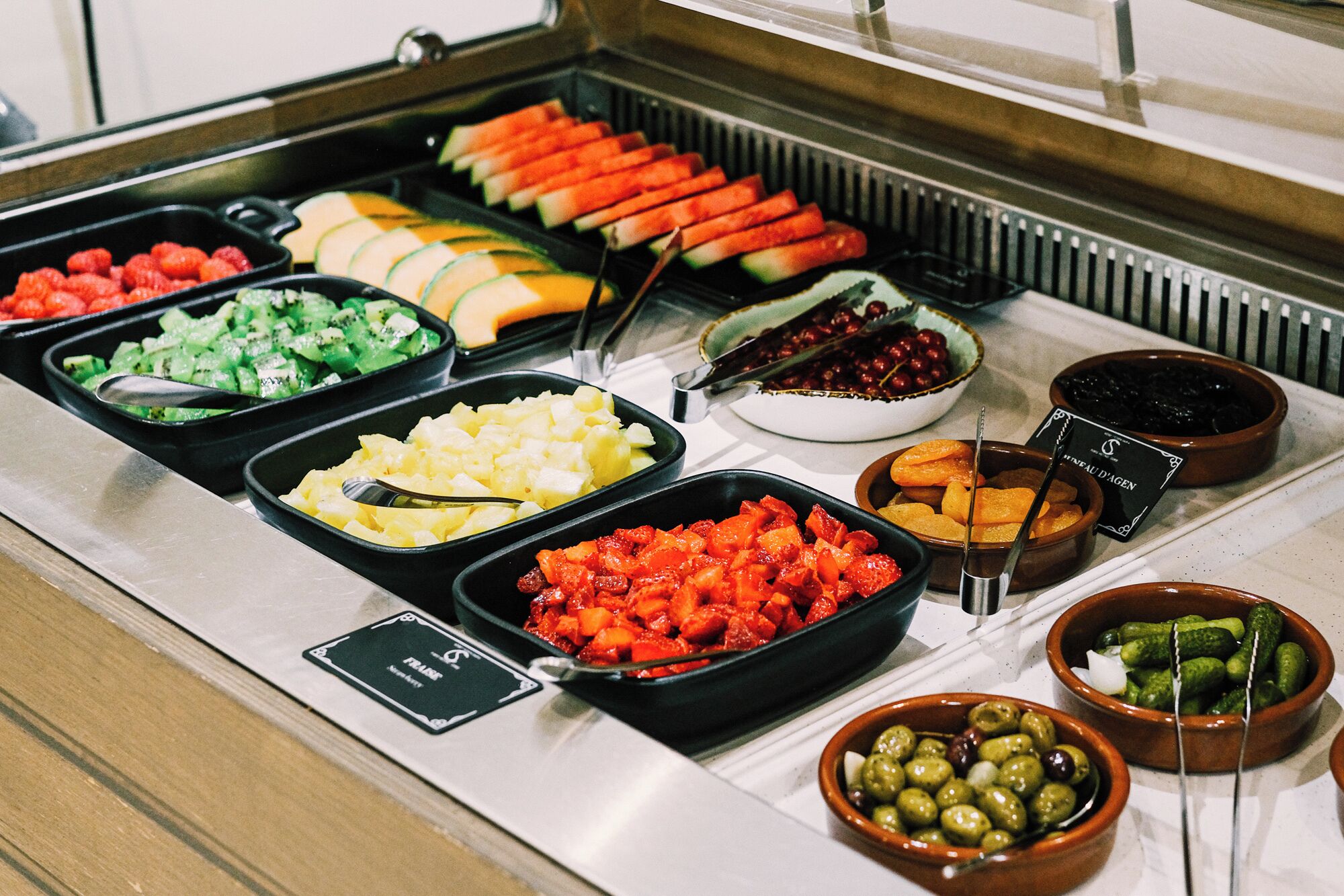 Un bufé con diversas opciones de comida, incluyendo frutas, verduras y salsas.