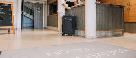 Zona de recepción de un hotel con mostrador de registro, una maleta negra y un cartel que dice 'HOTEL COSTA SALINA'.