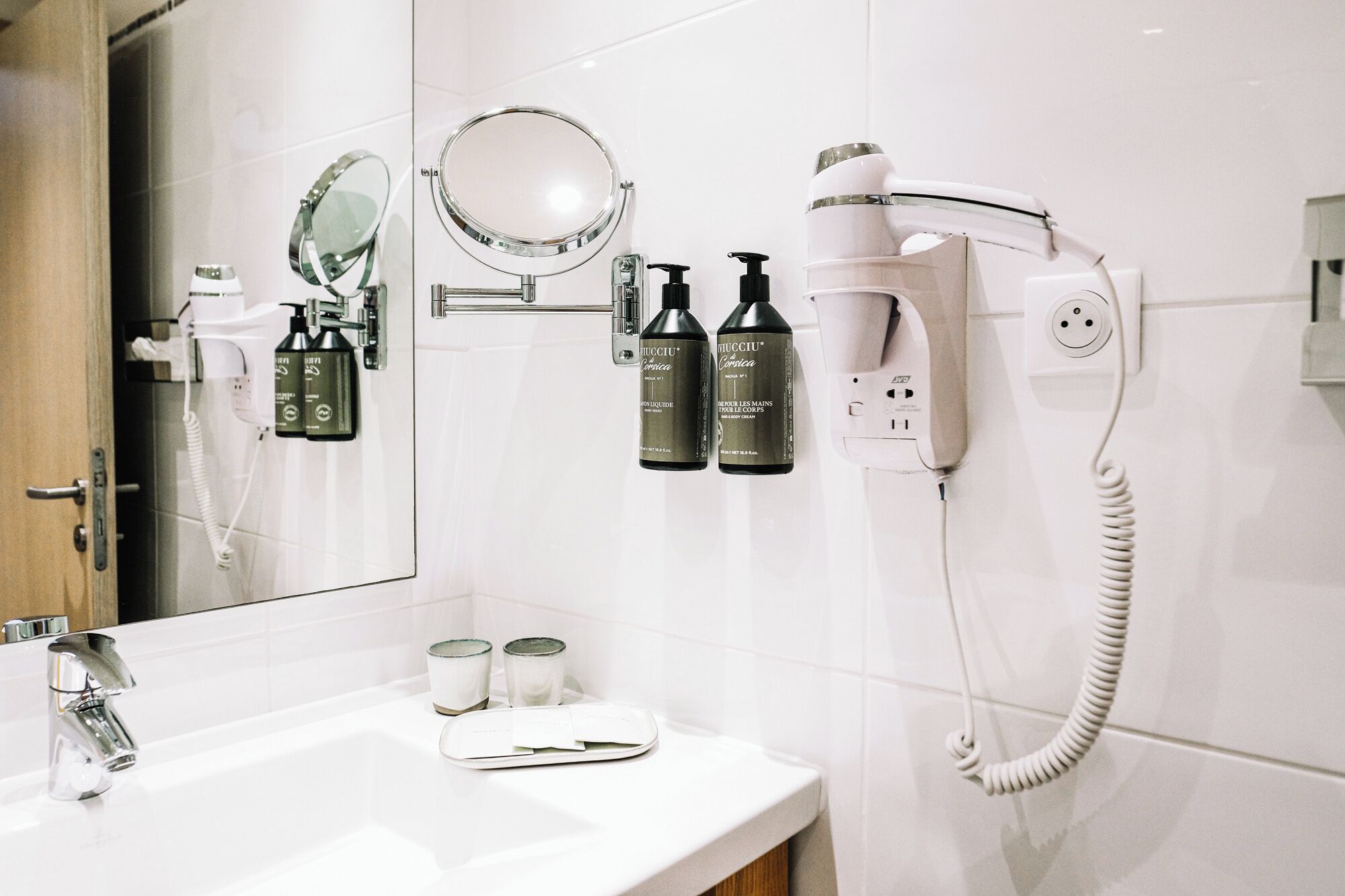 A bathroom with a white sink, a mirror, a hairdryer, and two bottles of hair care product.