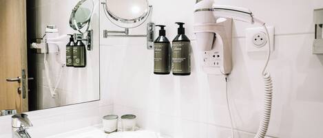 A bathroom with a white sink, a mirror, a hairdryer, and two bottles of hair care product.