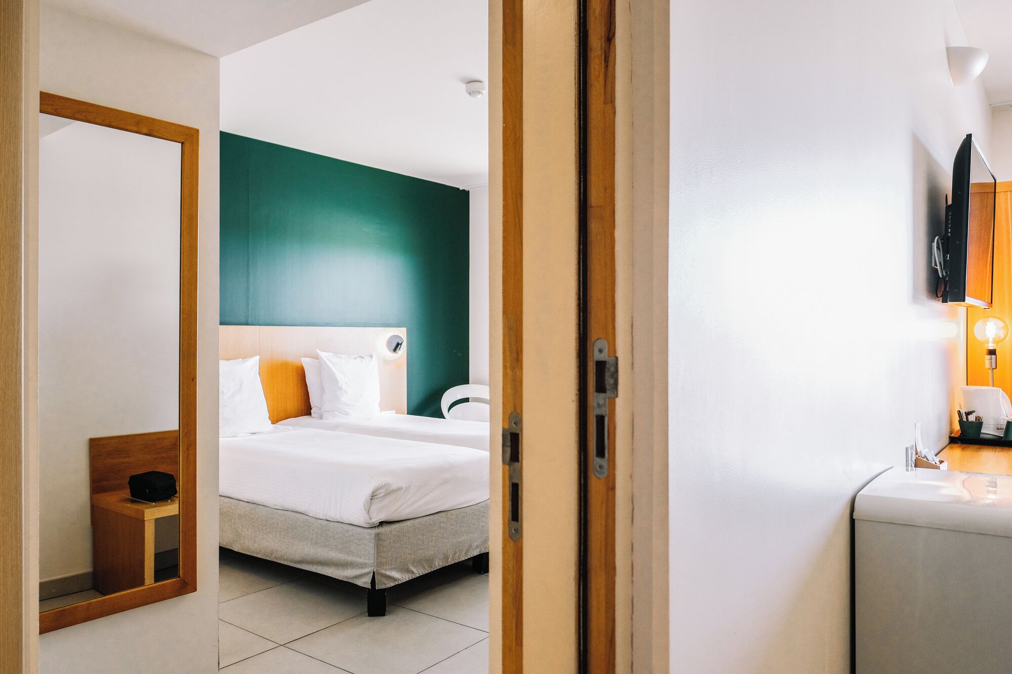Una habitación de hotel con cama, mesita de noche con lámpara y espejo.