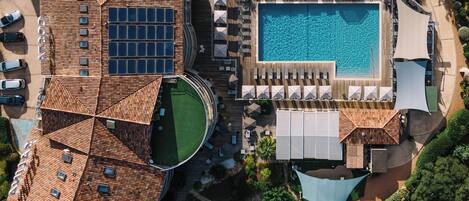 An aerial view of a resort with a swimming pool, sun loungers, and a rooftop with solar panels.