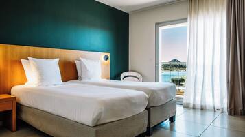 A hotel room with two beds, a nightstand, a chair, and a balcony with a view of the sea.
