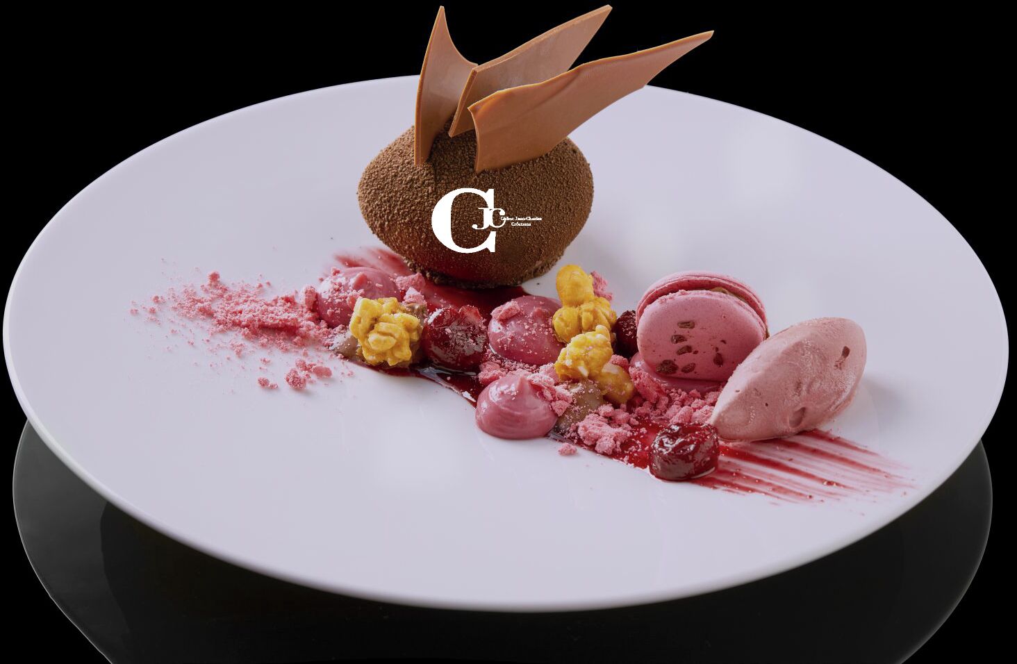 Un dessert composé d’une sphère de chocolat, de macarons et de fruits rouges, le tout présenté sur une assiette blanche.