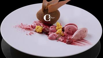 Un dessert composé d’une sphère de chocolat, de macarons et de fruits rouges, le tout présenté sur une assiette blanche.