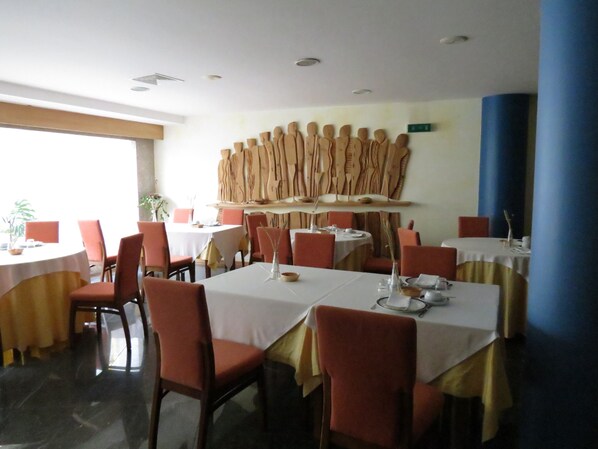 A restaurant with round tables, red chairs, and a unique wooden sculpture on the wall.