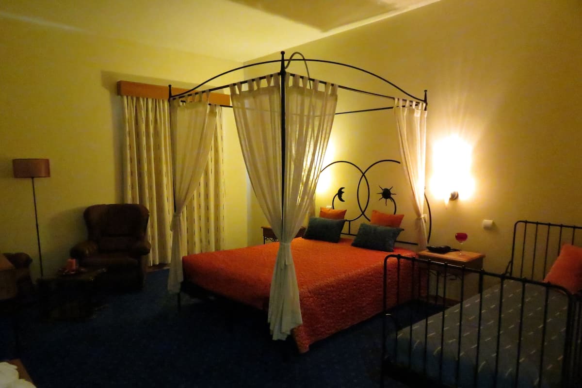 A room with a four-poster bed, a chair, a nightstand, and a lamp.