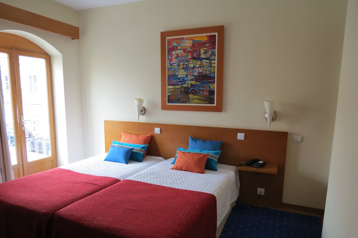 A hotel room with two beds, a painting on the wall, and a phone on the nightstand.