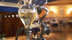 Una botella de vino sobre un soporte decorativo, con uvas y un sacacorchos.