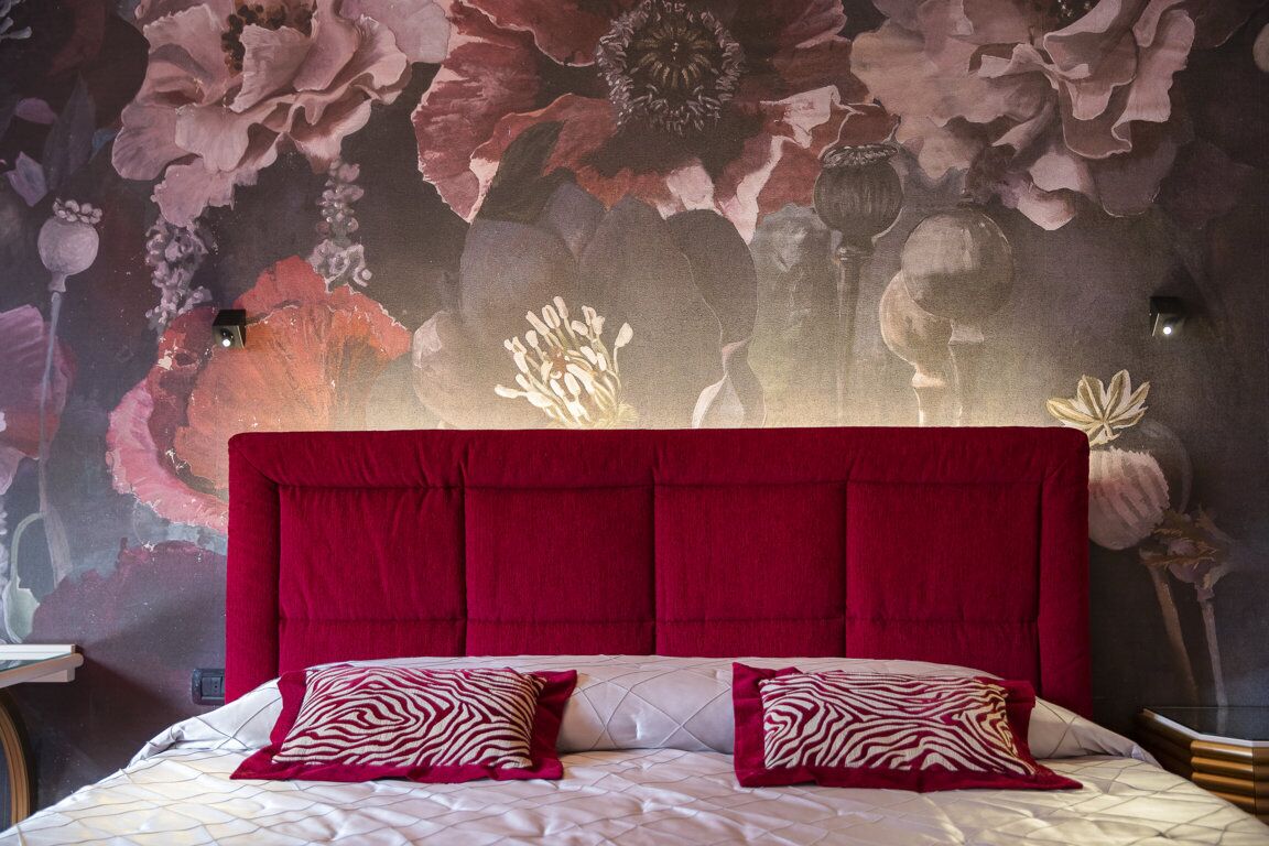 Una cama con cabecera roja, dos almohadas estampadas y un mural floral en la pared de fondo.