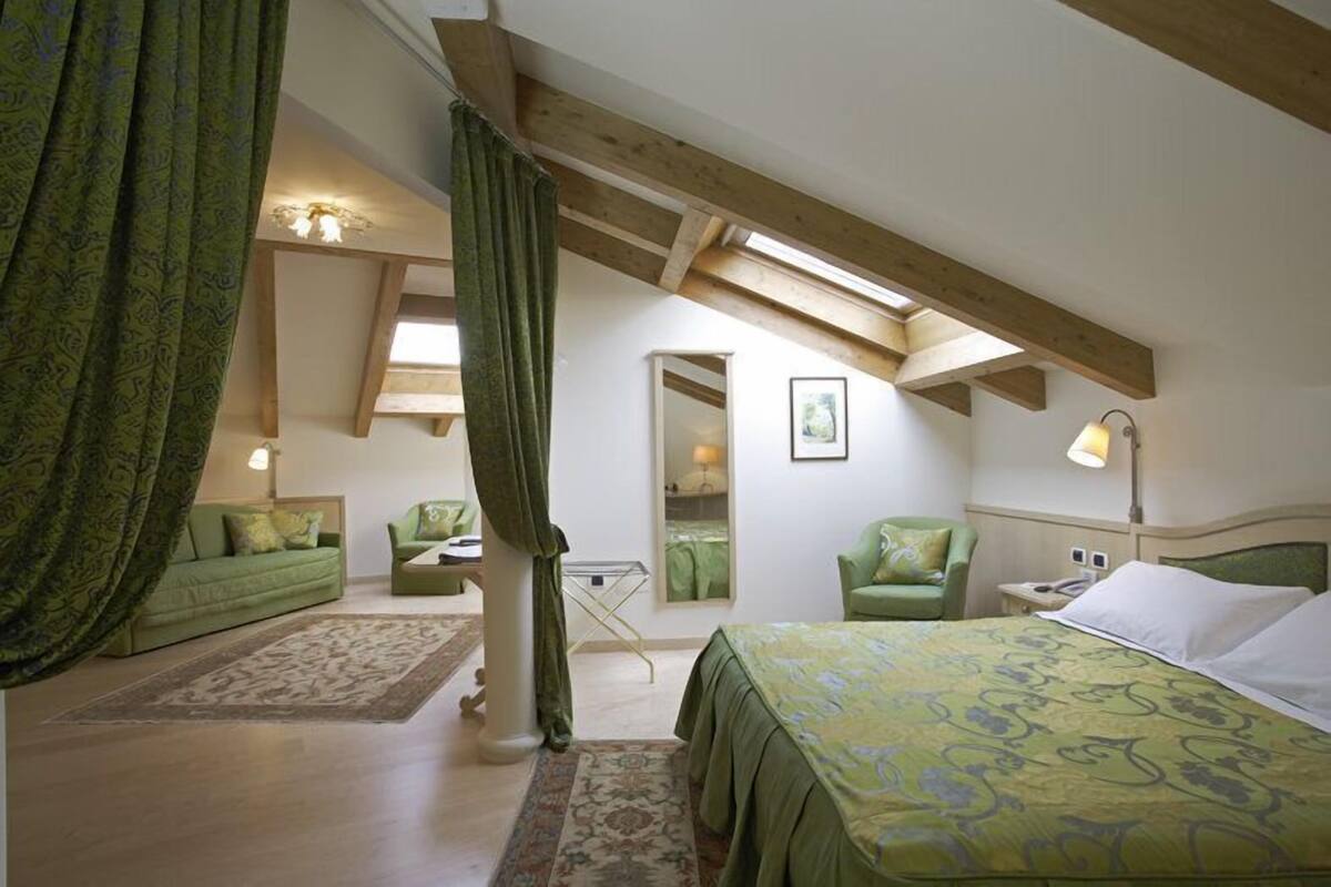A bedroom with a bed, a green sofa, a chair, a small table, and a nightstand.