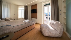 Habitación de hotel con cama, una silla, un otoman mullido, televisor y vistas al exterior.