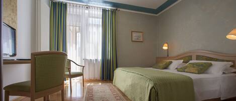 Ein Hotelzimmer mit Bett, einem Sessel, einem Schreibtisch mit Computer und einem Fenster mit Vorhängen.