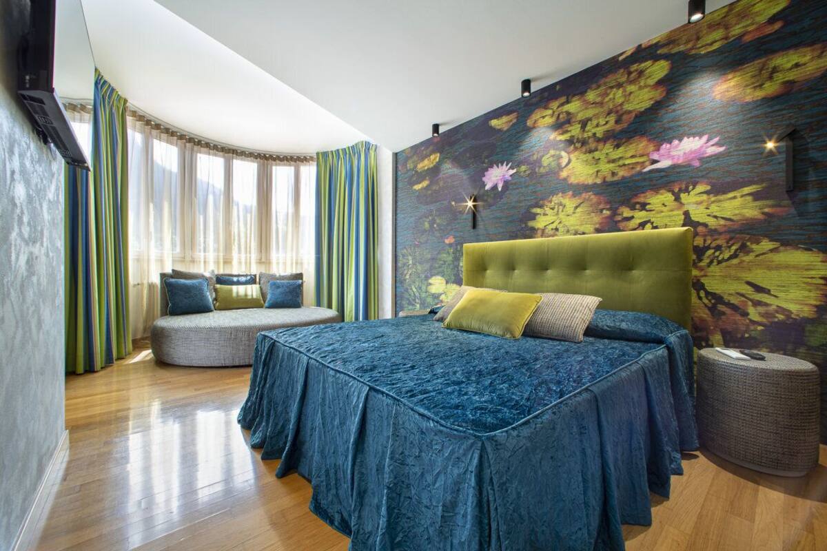 A bedroom with a large bed, a curved bench, and a wall mural.