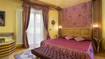 Quarto com cama grande, cabeceira de madeira, um banquinho, radiador, cortinas e parede estampada.