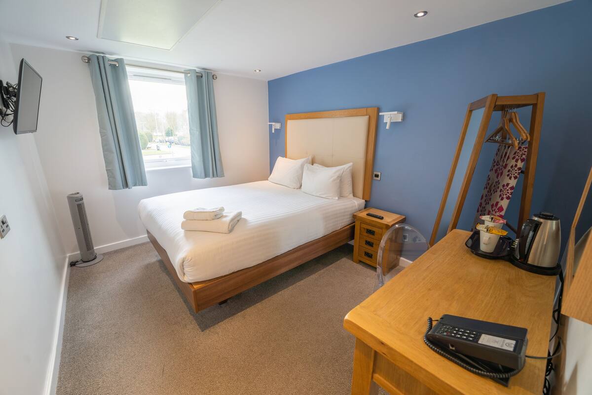 Ein Hotelzimmer mit Bett, Nachttisch und Schreibtisch mit Telefon.